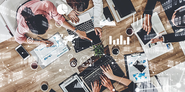An overhead view of a diverse group of people working together at a wooden table with laptops and documents.